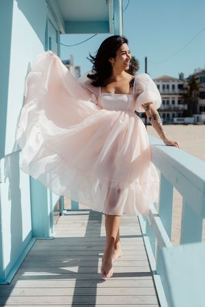Woman in flowing white dress twirling on blue boardwalk by beach.