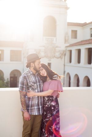 A couple embraces during golden hour in front of a white Spanish-style building.