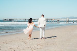 Couple walking hand in hand along sunny beach shoreline.