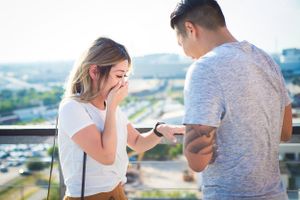 Emotional reaction during surprise proposal on urban rooftop with cityscape view.