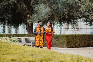 Couple in red and yellow outfits walking through garden setting.