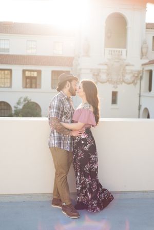 A couple in casual attire embraces during golden hour with Spanish architecture in the background.