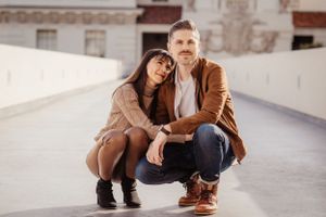 A couple in brown jackets poses together on a white terrace.