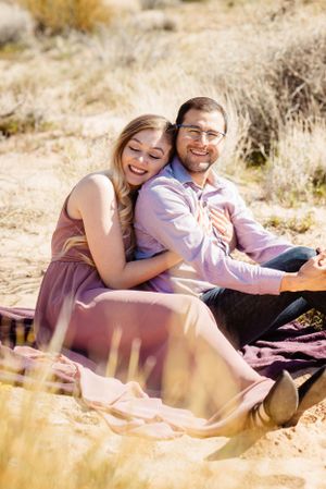 A couple lounges together on a blanket in a desert setting during a photo session.