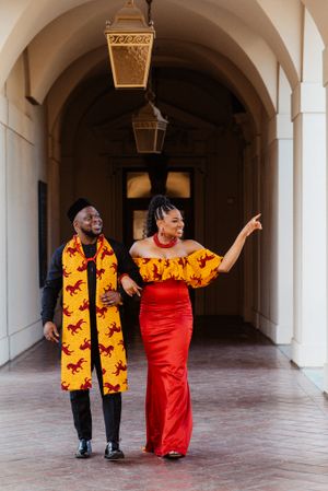 Couple dancing in a courtyard with woman in red dress and yellow floral print accessories.