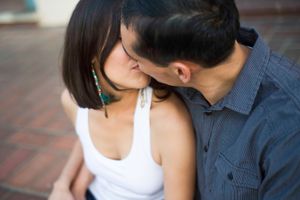 Two people share a close moment while sitting on brick pavement during an outdoor photoshoot.