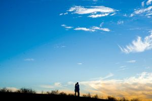 Silhouettes against a vibrant blue sky with scattered white clouds at sunset.