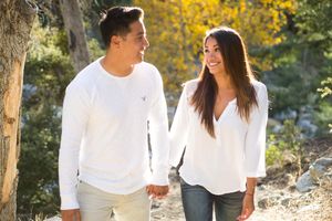 A couple wearing coordinated white outfits poses together against a backdrop of yellow flowers and trees.