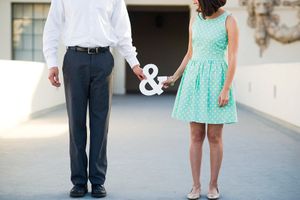 A couple walks together on a concrete path, with one wearing a mint green dress and the other in formal attire.