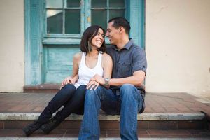 A couple sits casually together on a porch with turquoise window frames and cream-colored walls.