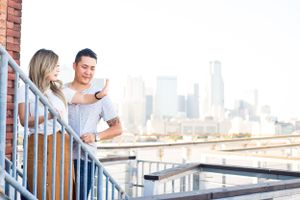 Couple looking at phone together on urban balcony with downtown view.