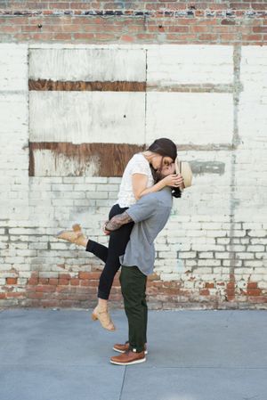 A romantic couple poses playfully against a brick wall backdrop in a series of candid shots.