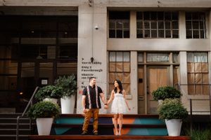 A couple poses on green steps outside an industrial building entrance.