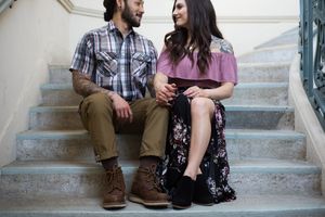 A couple shares tender moments while sitting on concrete steps outdoors.