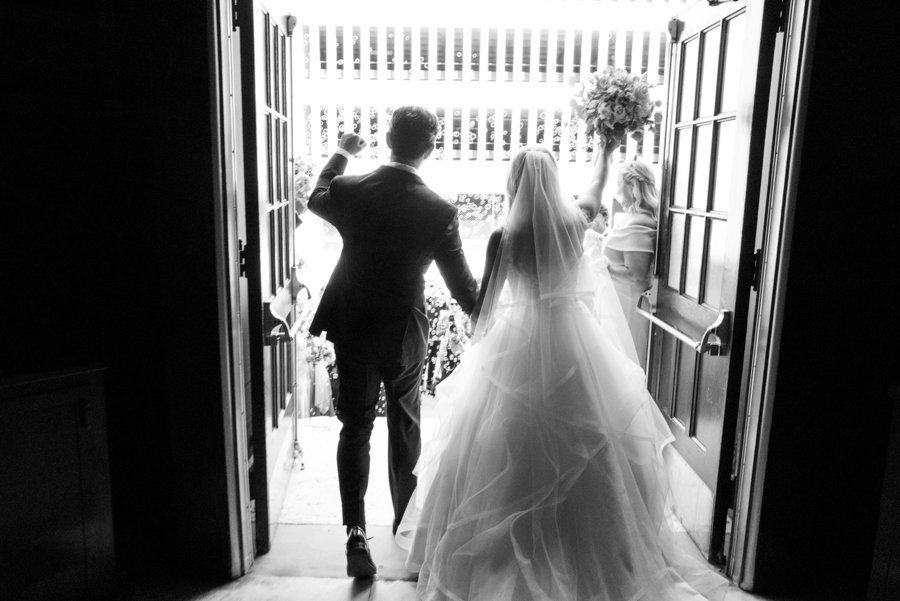 Silhouette of newlyweds walking through church doors into bright sunlight.