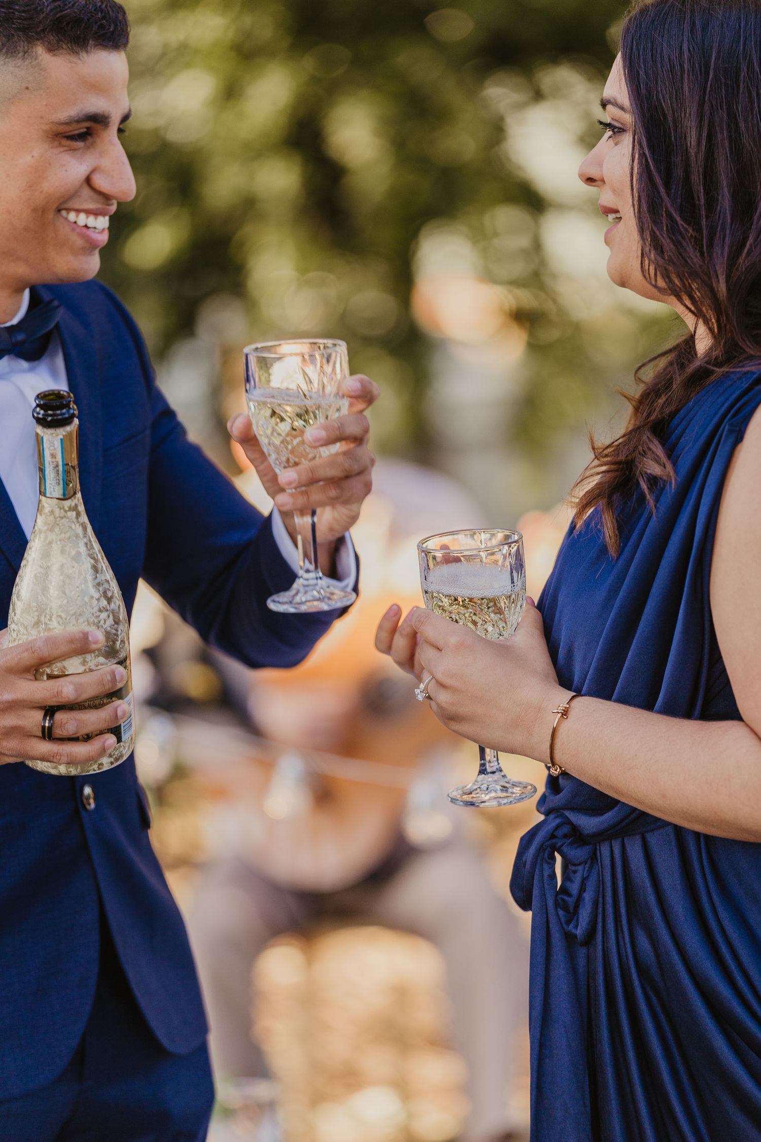 Couple in formal attire shares champagne during outdoor celebration.