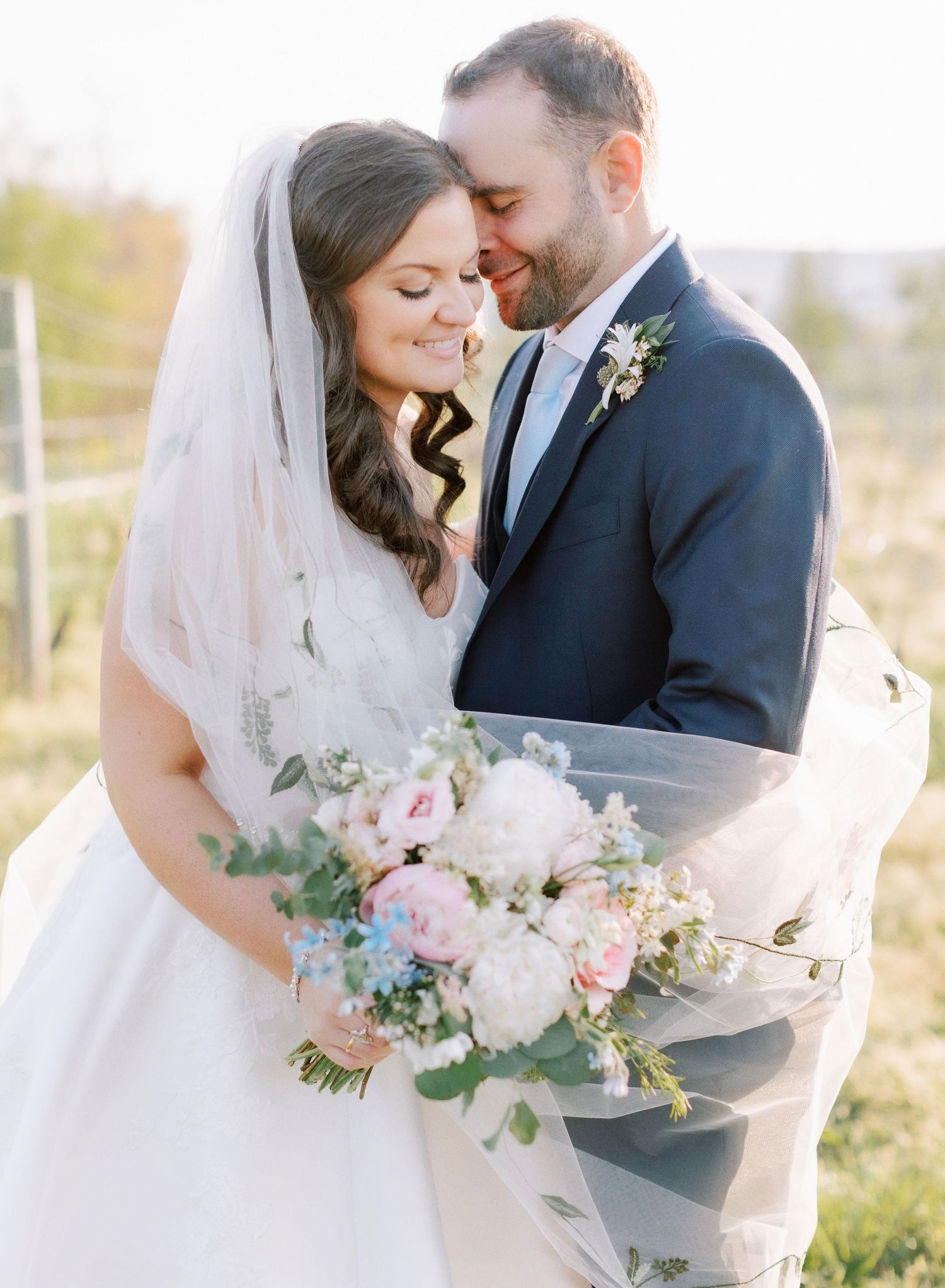 Wedding couple sharing intimate moment with pastel bouquet in outdoor setting.