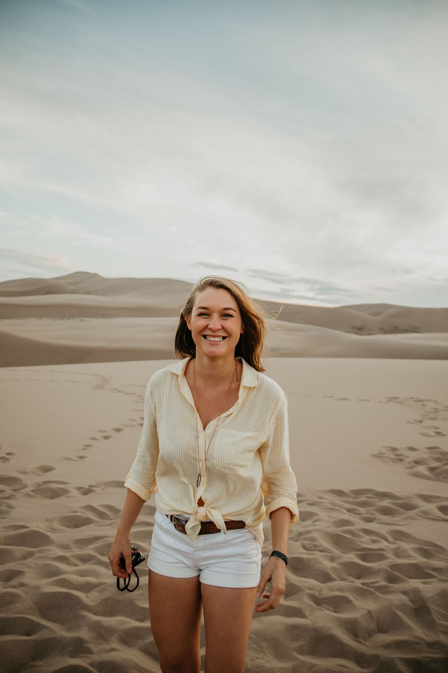 Person enjoying a playful moment on sand dunes against a cloudy sky.