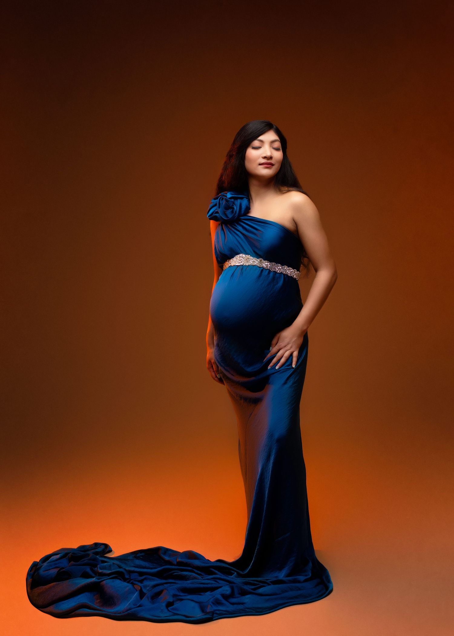 an expecting mother stands soaking in the moment wearing a sliky blue dress