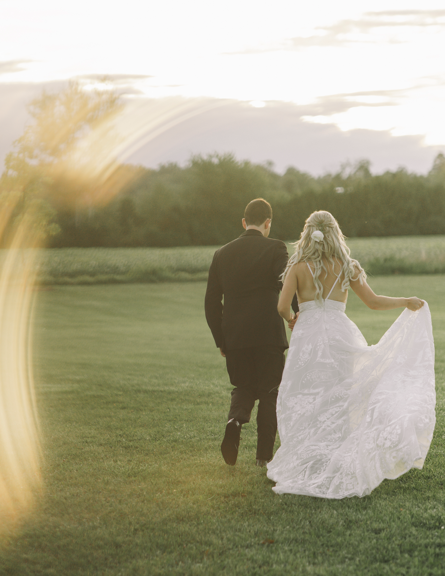 Couple running through green field at sunset with flowing white wedding dress.