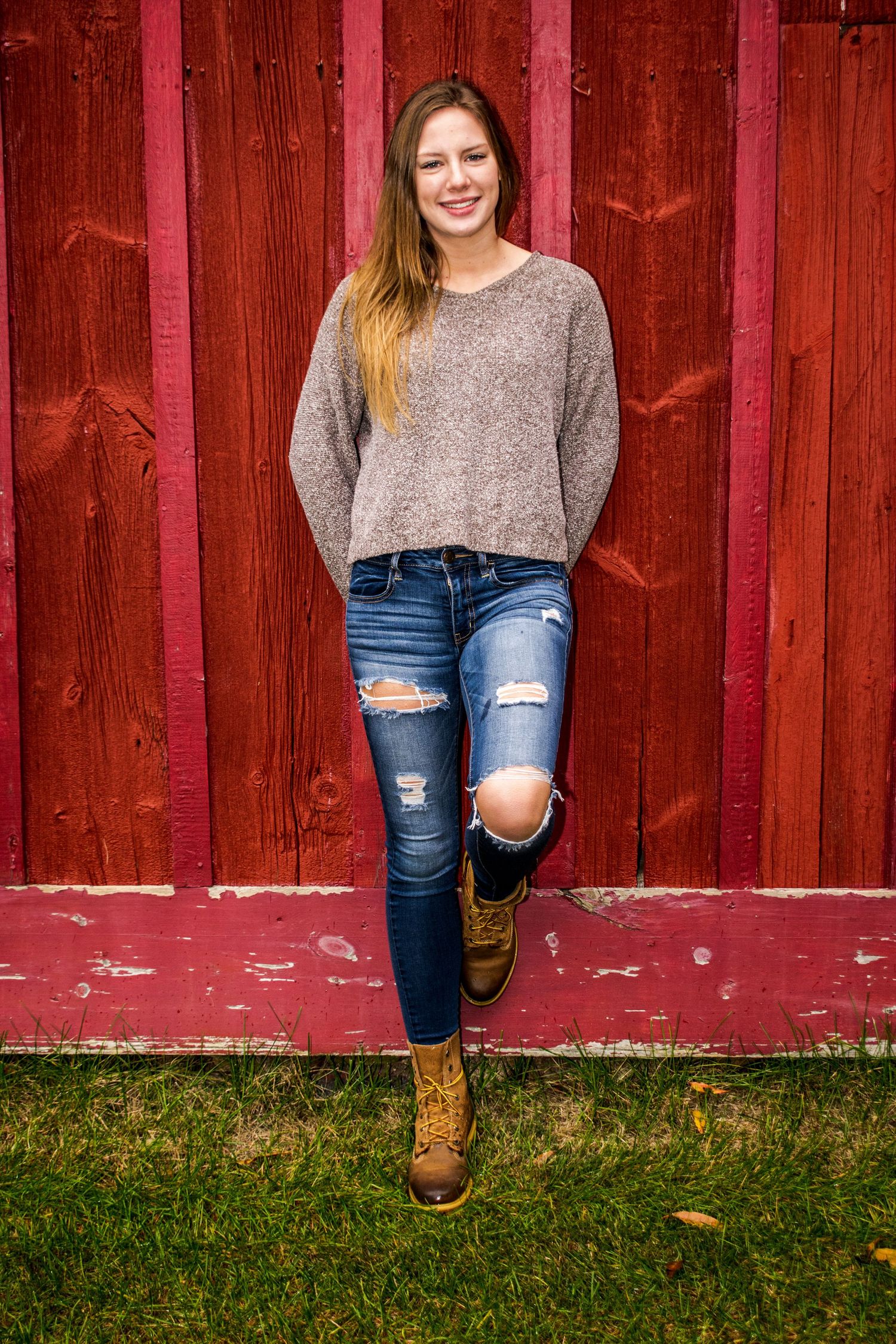 Stylish outfit featuring distressed jeans and boots against red barn wall.