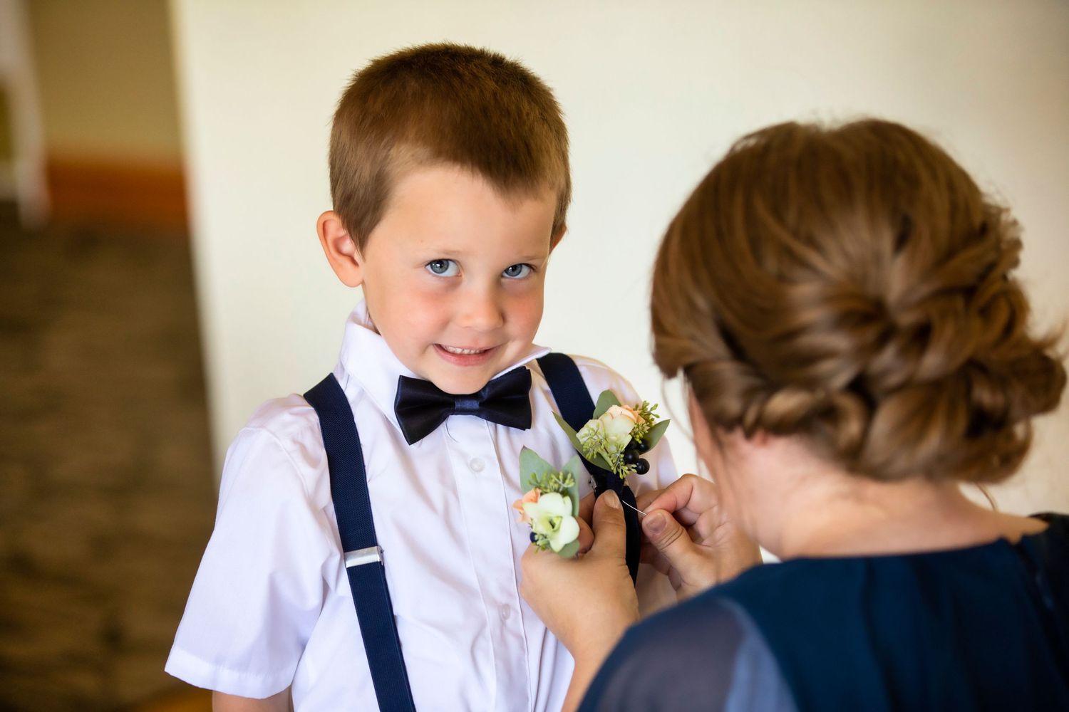 A sweet moment as a boutonniere is pinned onto a white dress shirt with suspenders and bow tie.