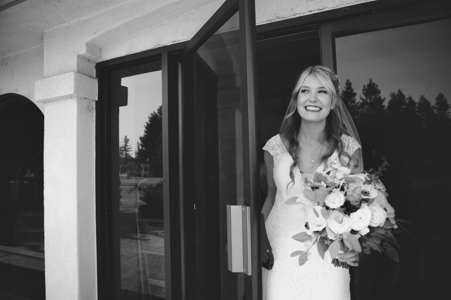 Black and white portrait of someone in a wedding dress holding a bouquet by a doorway.