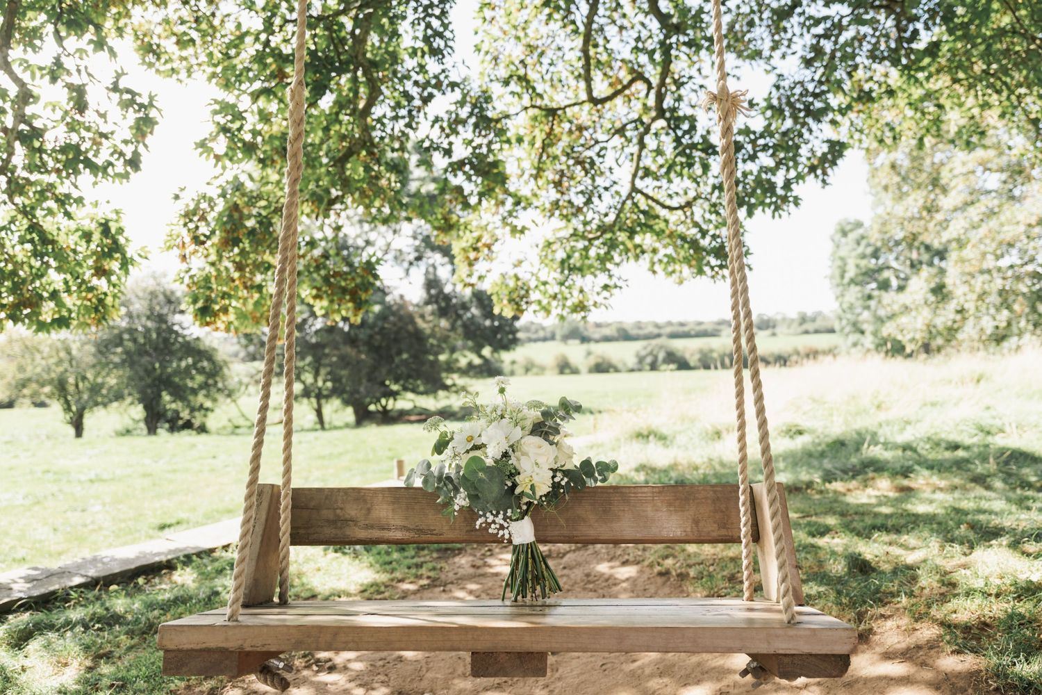 Rustic wooden swing decorated with flowers hanging in a sunny garden setting.