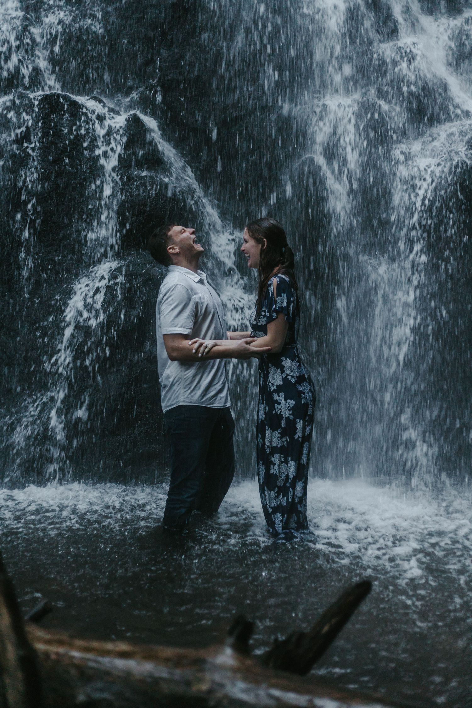 A couple shares an intimate moment while standing under a cascading waterfall.