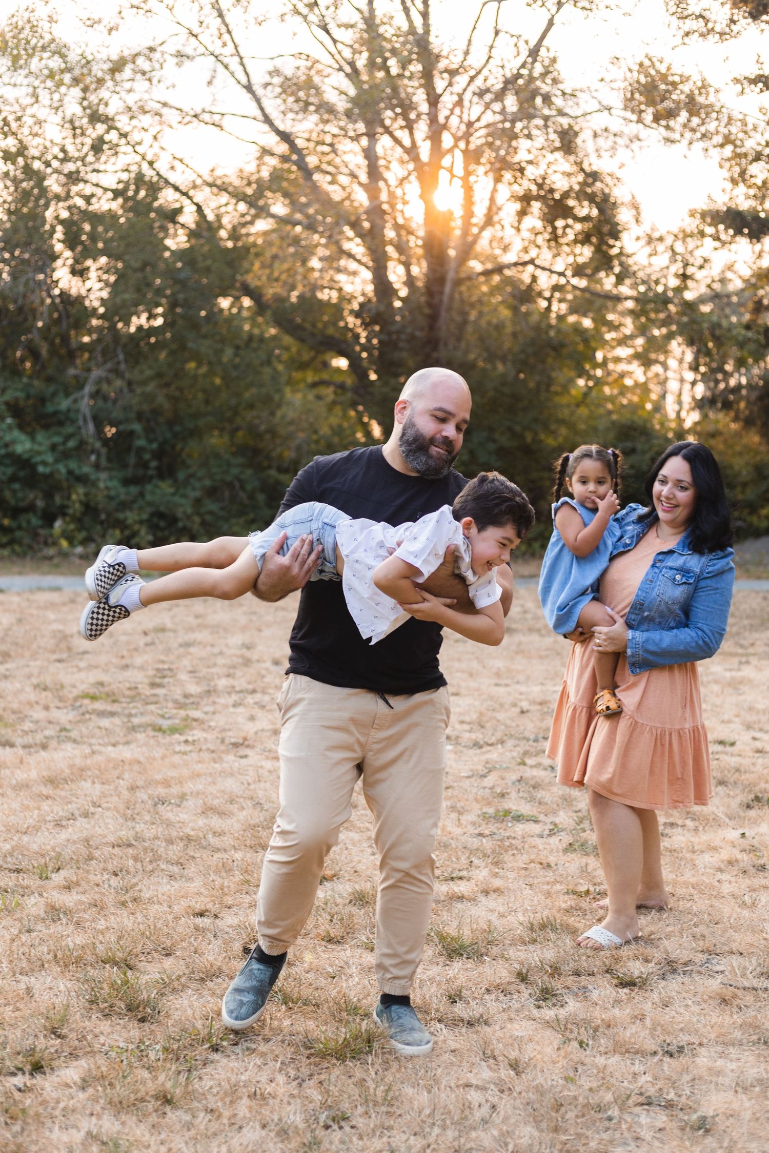 Playful family moment outdoors during golden sunset in grassy field.
