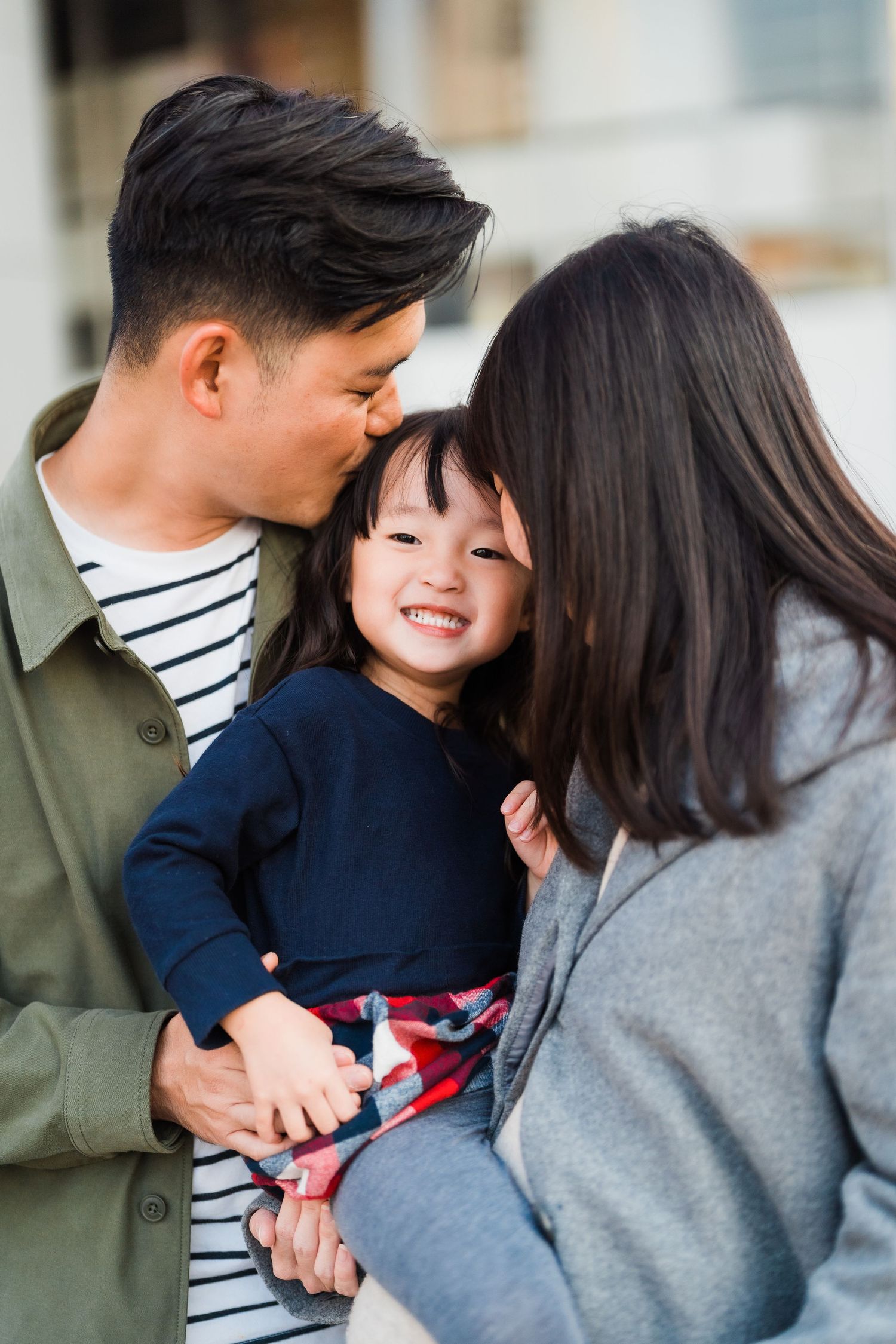 A loving family moment with parents embracing their smiling child wearing a navy sweater.