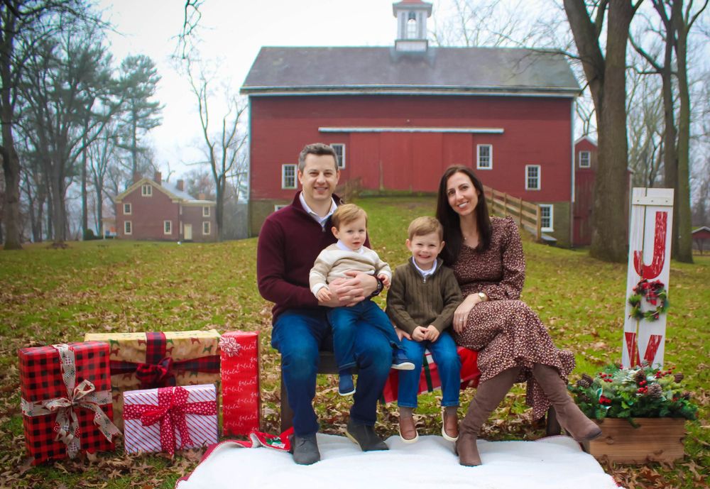 Family holiday photo session with wrapped presents and decorations by a red barn.