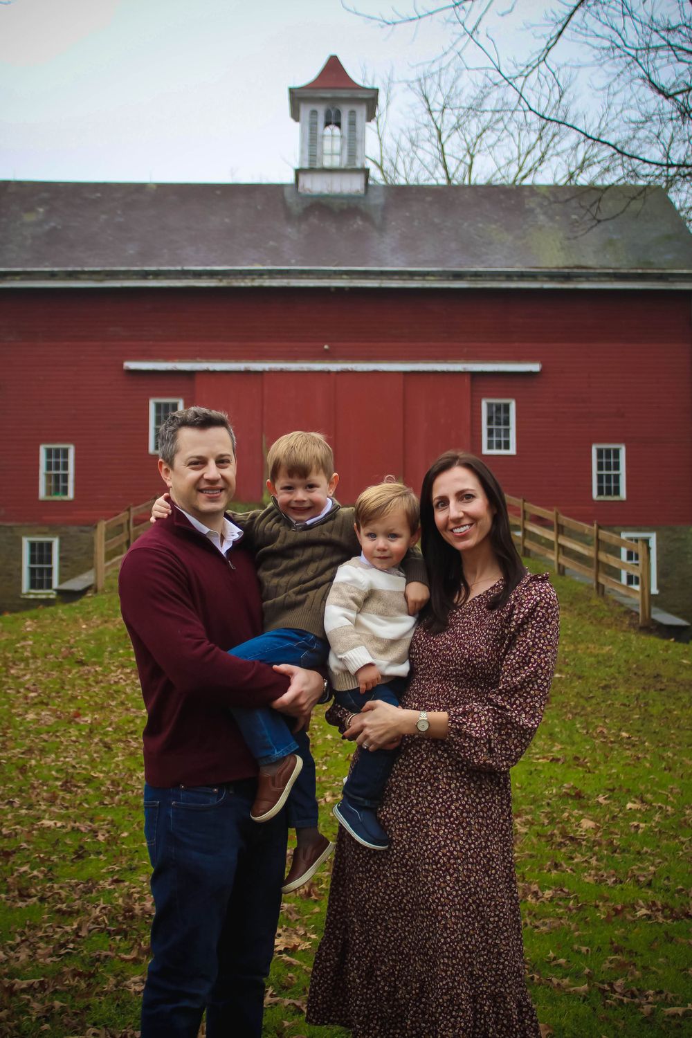Family portrait outside historic red barn with white cupola on an autumn day.
