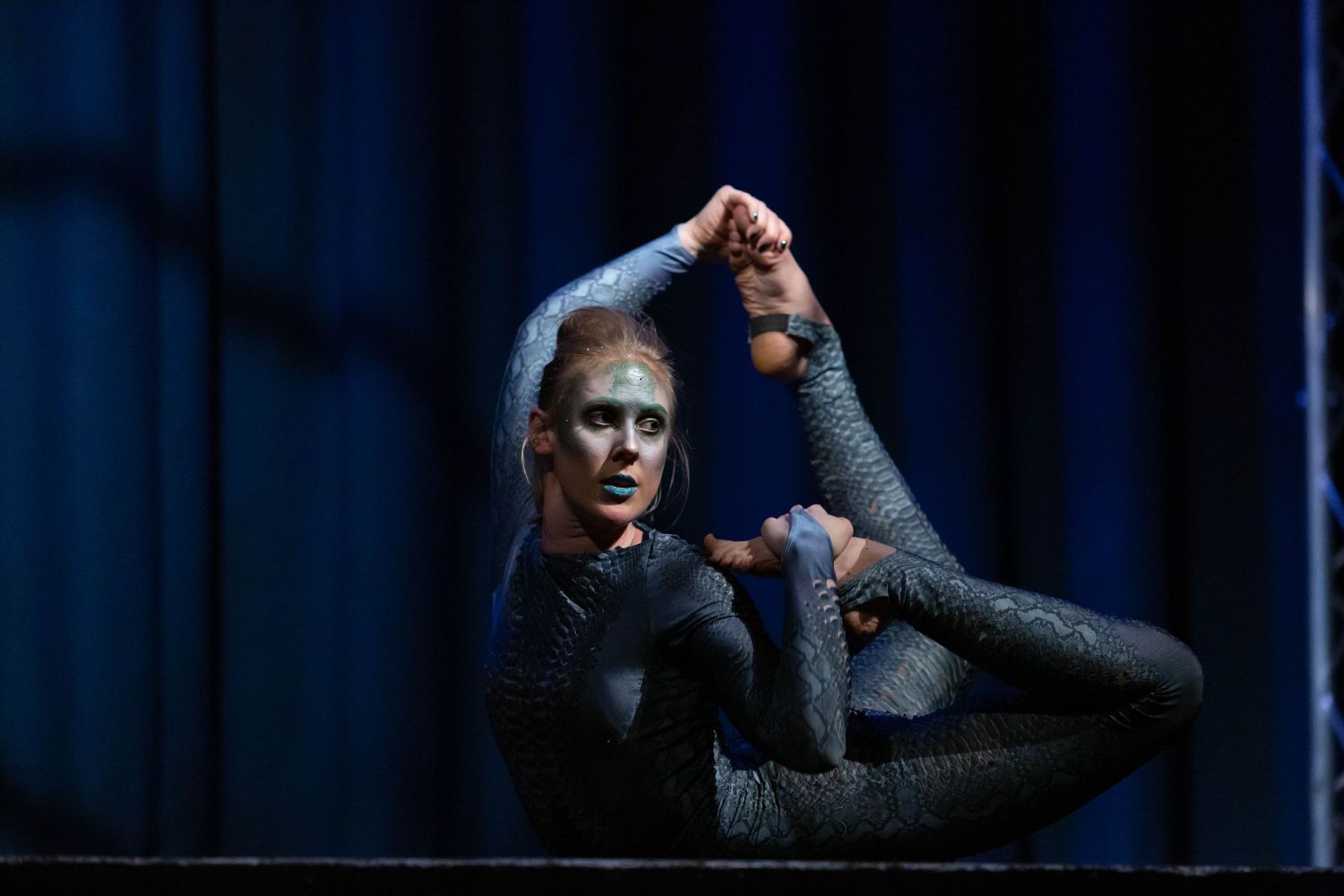 event photography of a contortion artist on a darkly lit stage wearing a snakeskin leotard