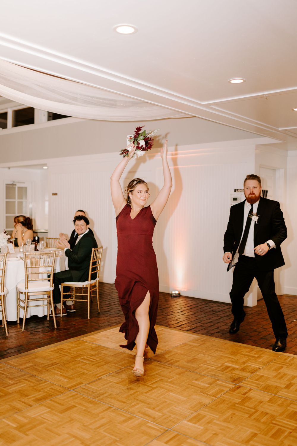 Wedding guests dance enthusiastically on wooden dance floor at indoor reception.