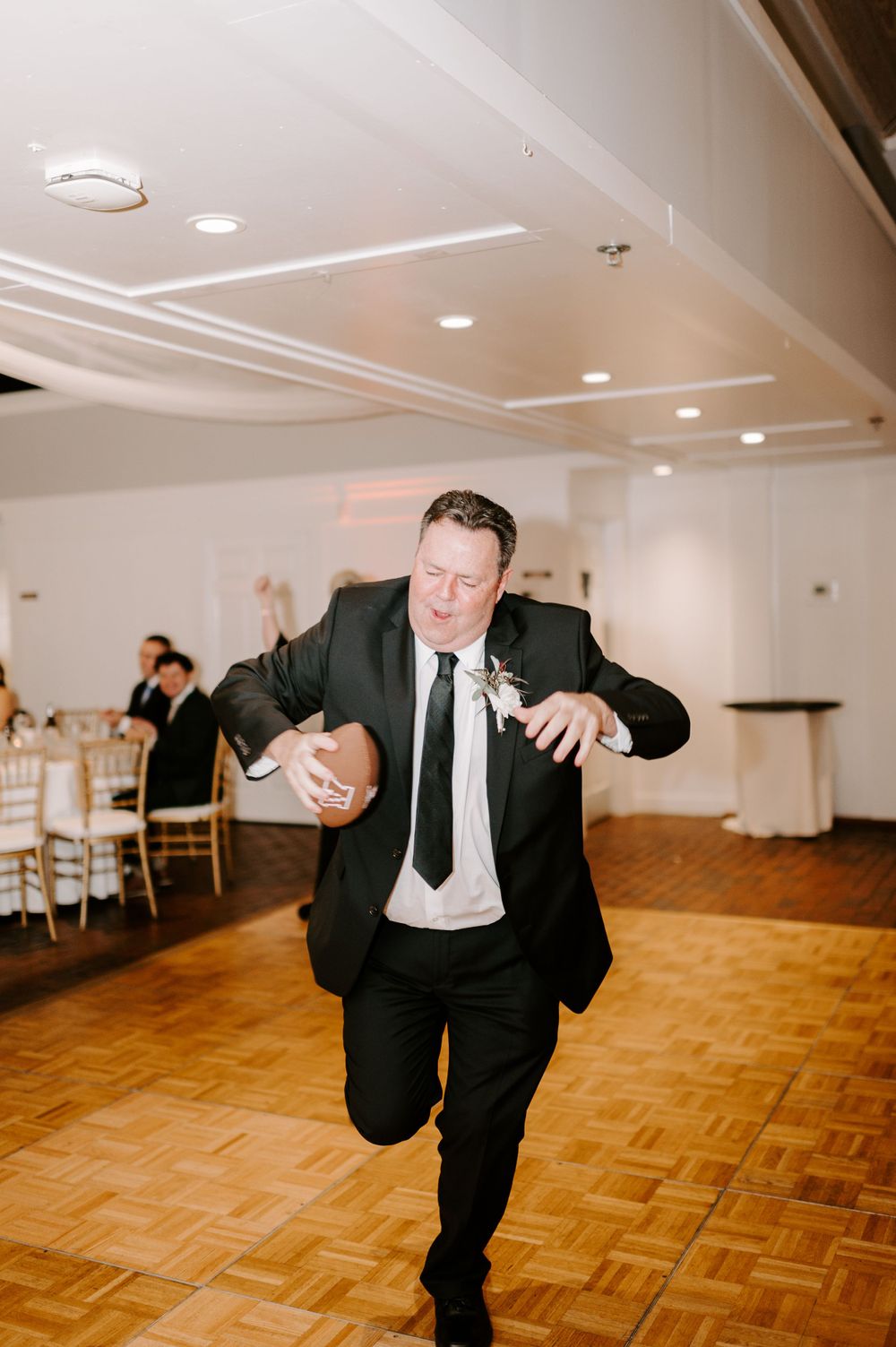 Wedding guest performs energetic dance moves across parquet floor at reception venue.