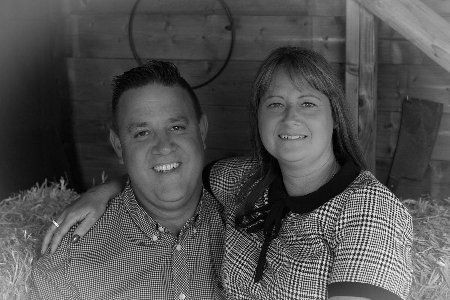 A rustic barn-style portrait of a couple sitting together on hay bales.