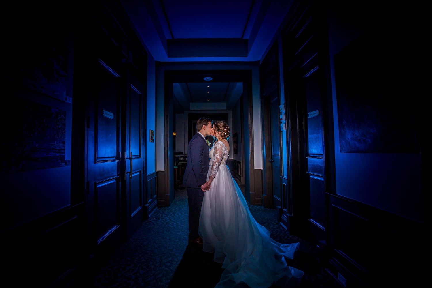 Dramatic blue-lit indoor wedding photos in a dark elegant hallway.
