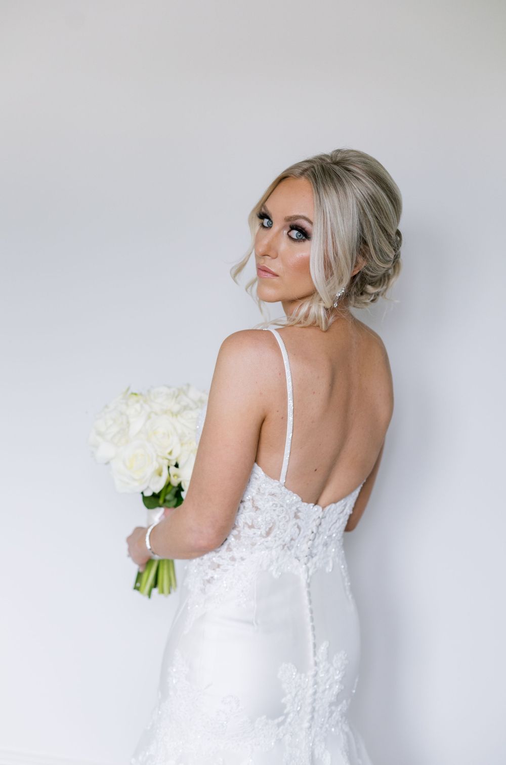 Back view of bride in fitted lace wedding gown holding white rose bouquet.