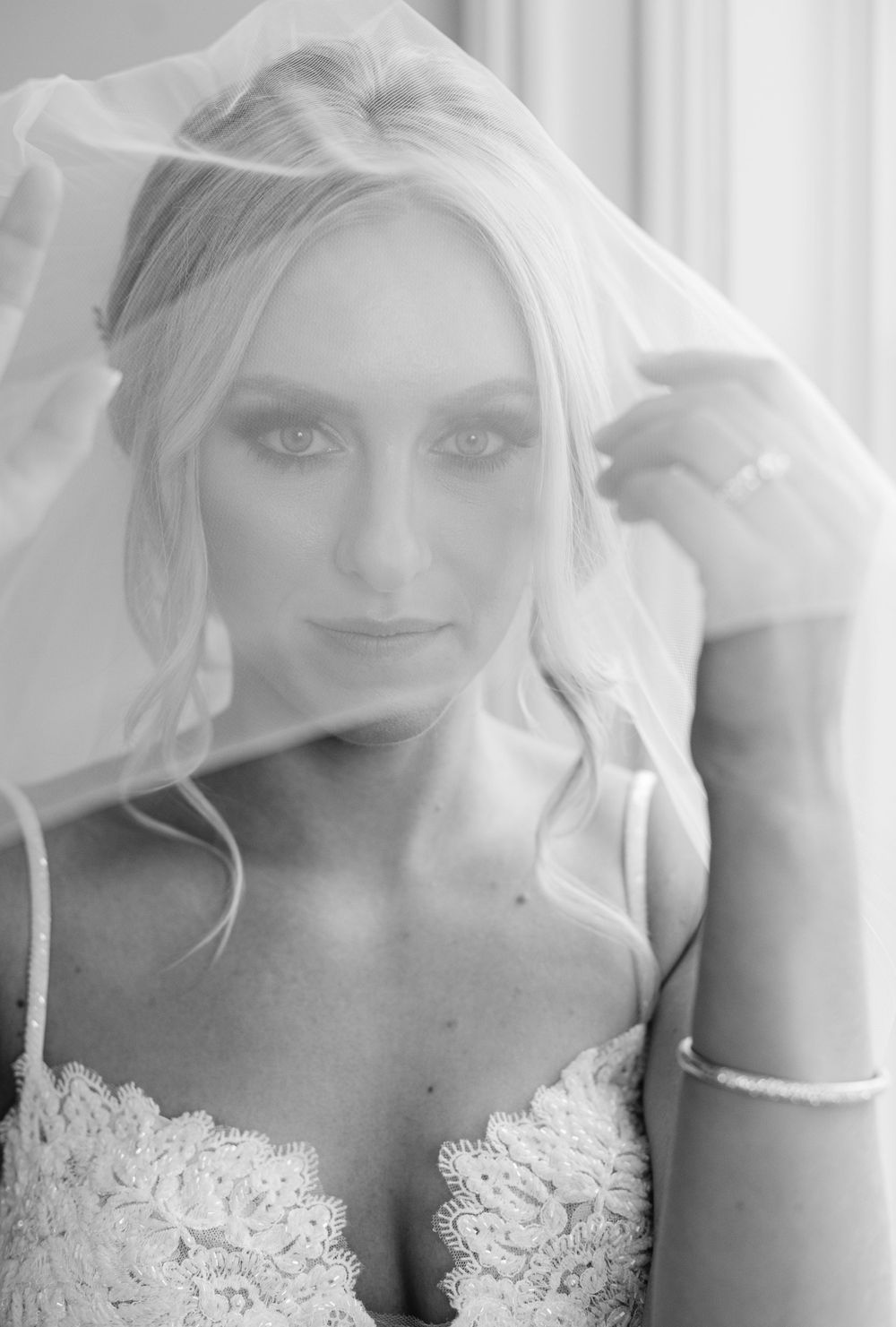 Close-up portrait of bride in lace dress with flowing veil in black and white photography.