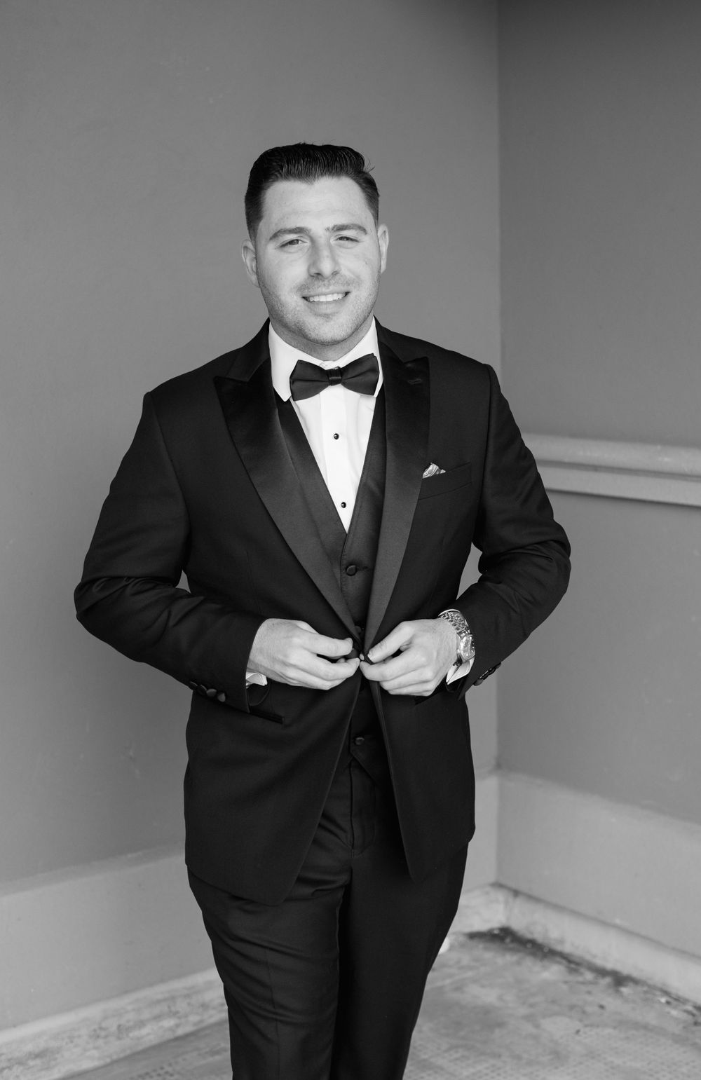 Black and white portrait of groom adjusting his tuxedo jacket.