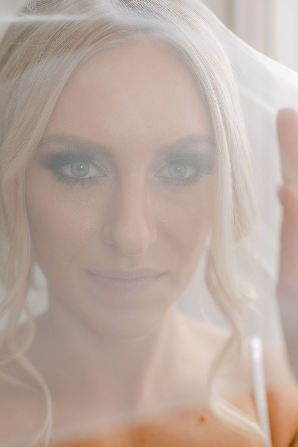 Ethereal close-up bridal portrait with smokey eye makeup through sheer wedding veil.
