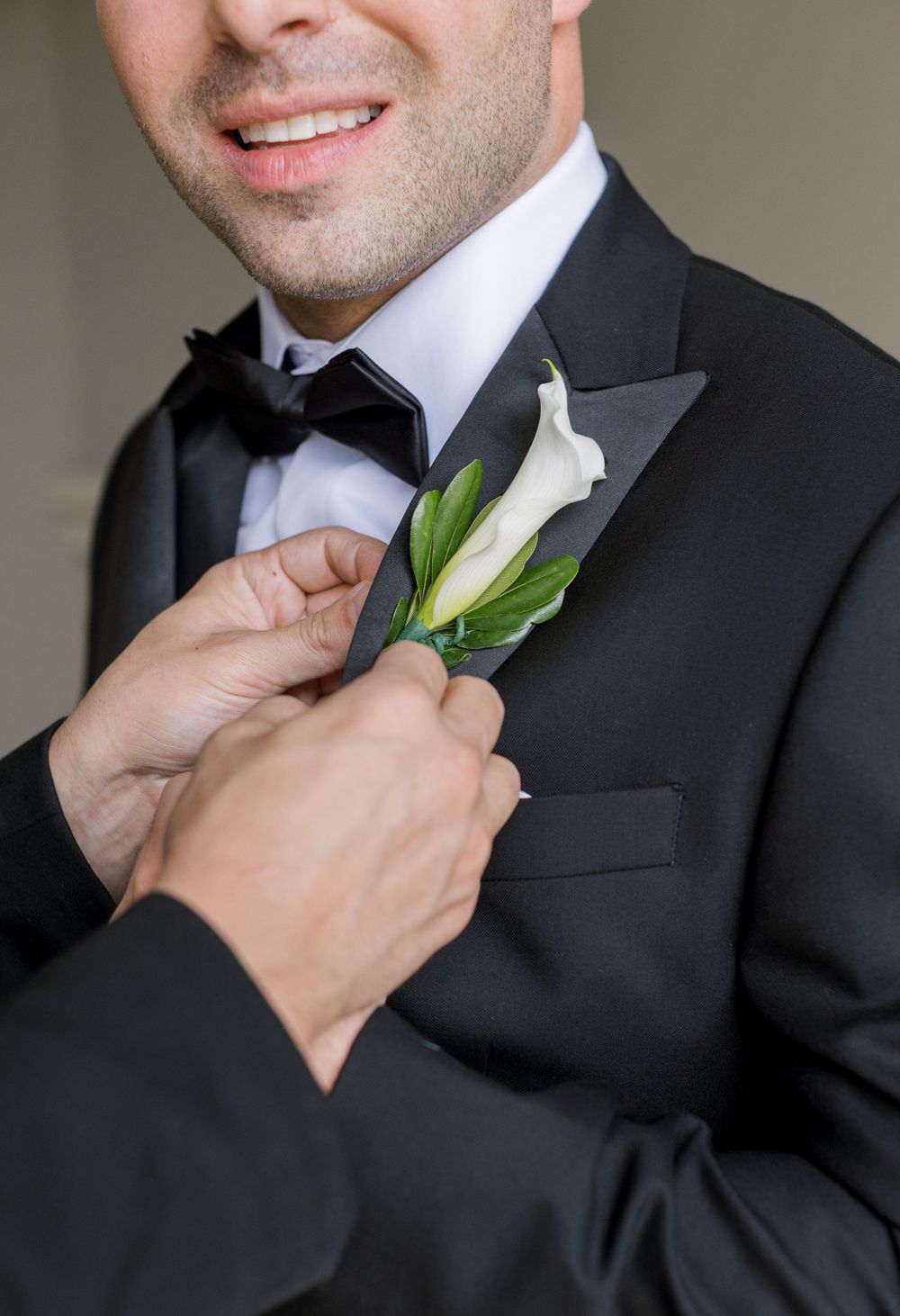 Hands pinning white calla lily boutonniere on groom's lapel.