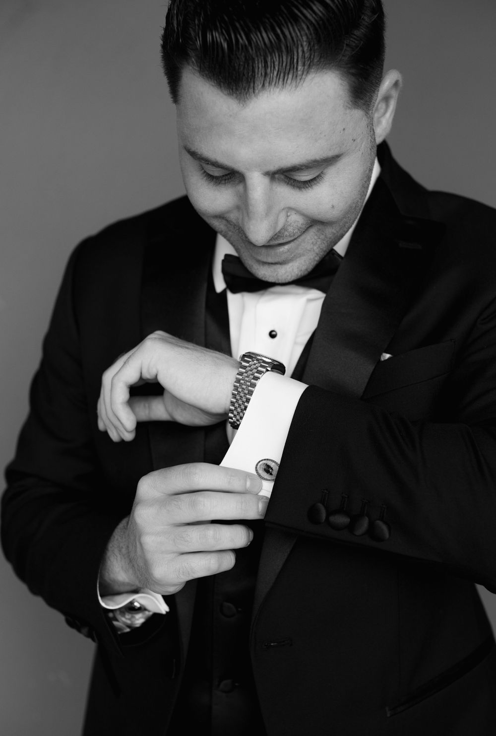 Groom in tuxedo adjusting cufflinks in black and white portrait.