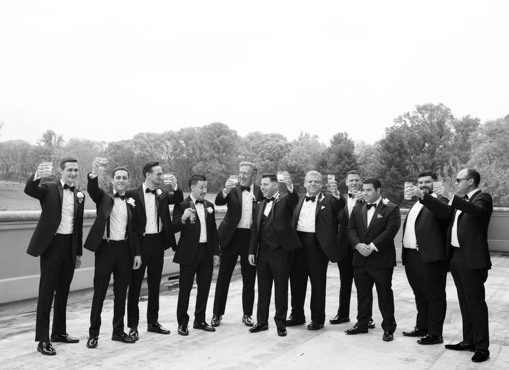 Groomsmen in black tuxedos posing outdoors in black and white photo.