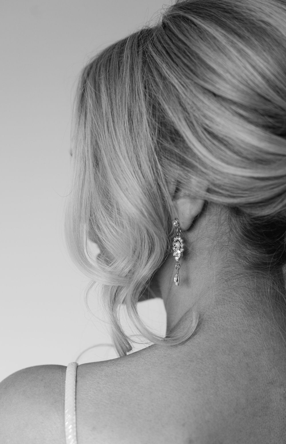 Close-up of blonde bridal hairstyle and dangling earring from behind.