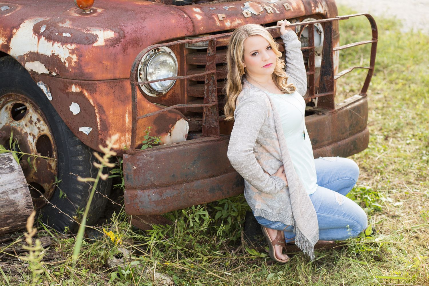 Person poses by vintage rusty truck grill in casual attire.