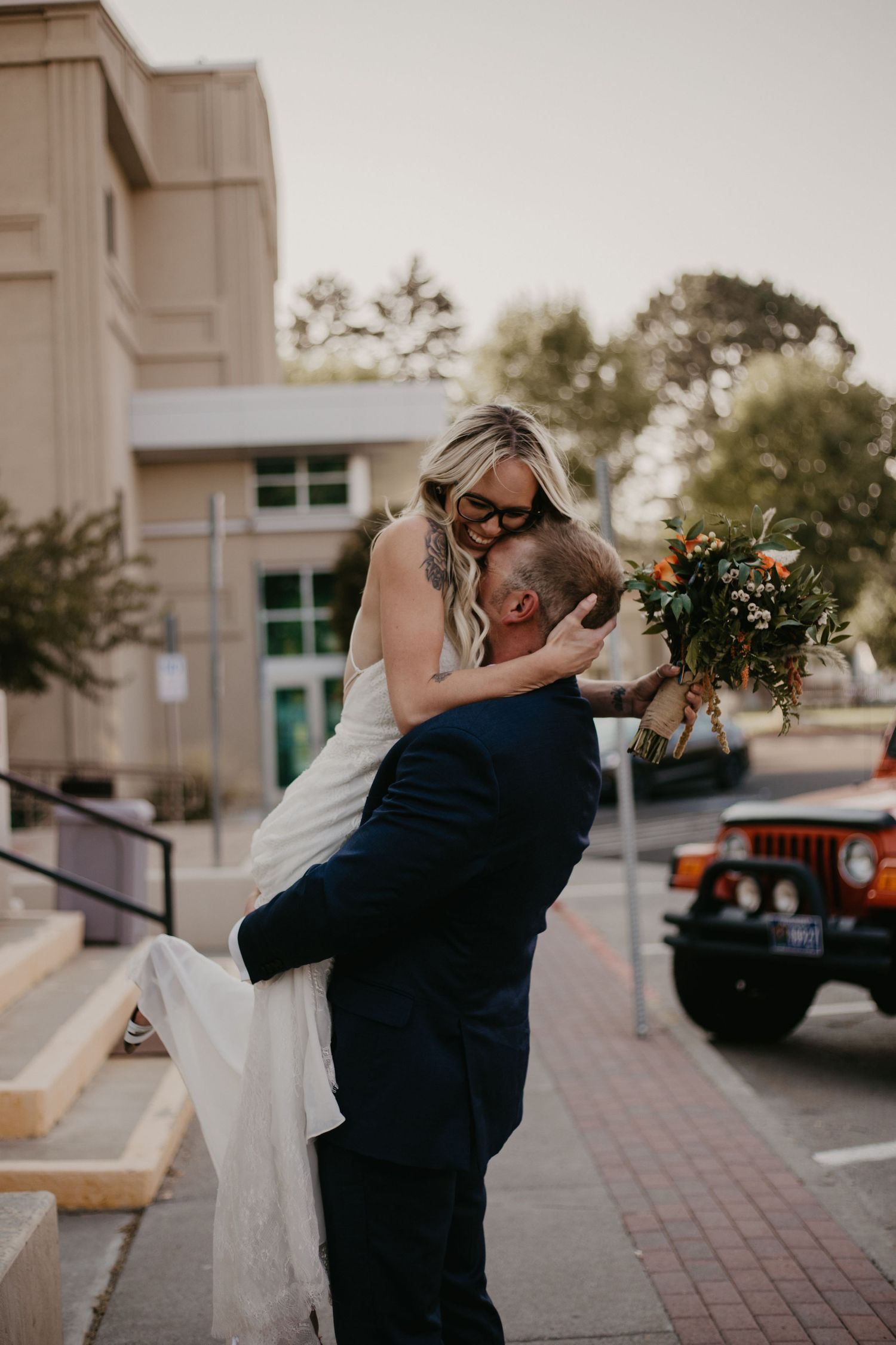 A playful wedding moment captured outside a building with a vintage Jeep in the background.