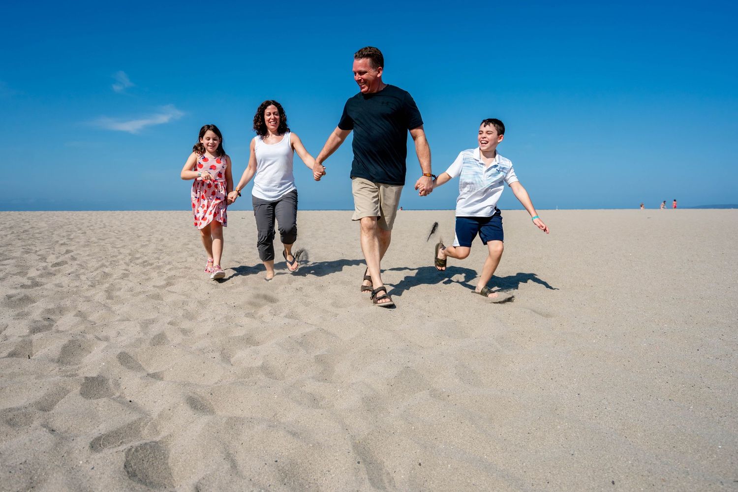 A happy family runs together on a sandy beach on a bright sunny day.