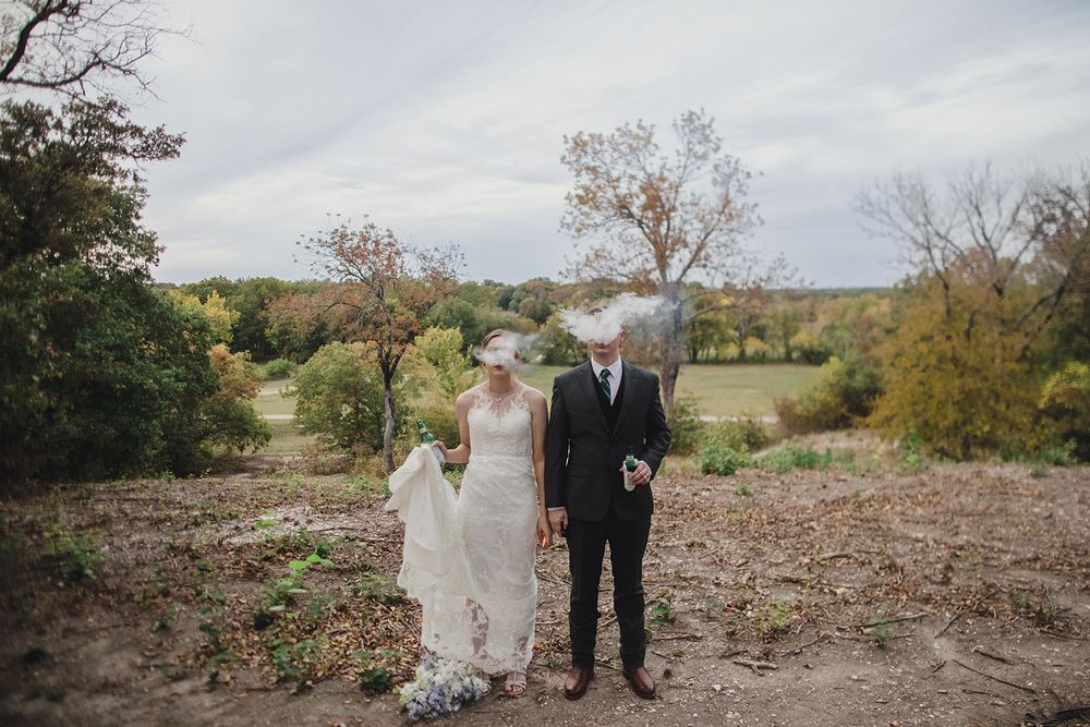 A couple in wedding attire stands together on a hilltop overlooking an autumn landscape.